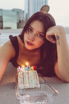 Portrait of a woman with birthday cake and candles outdoors, exuding style and allure.