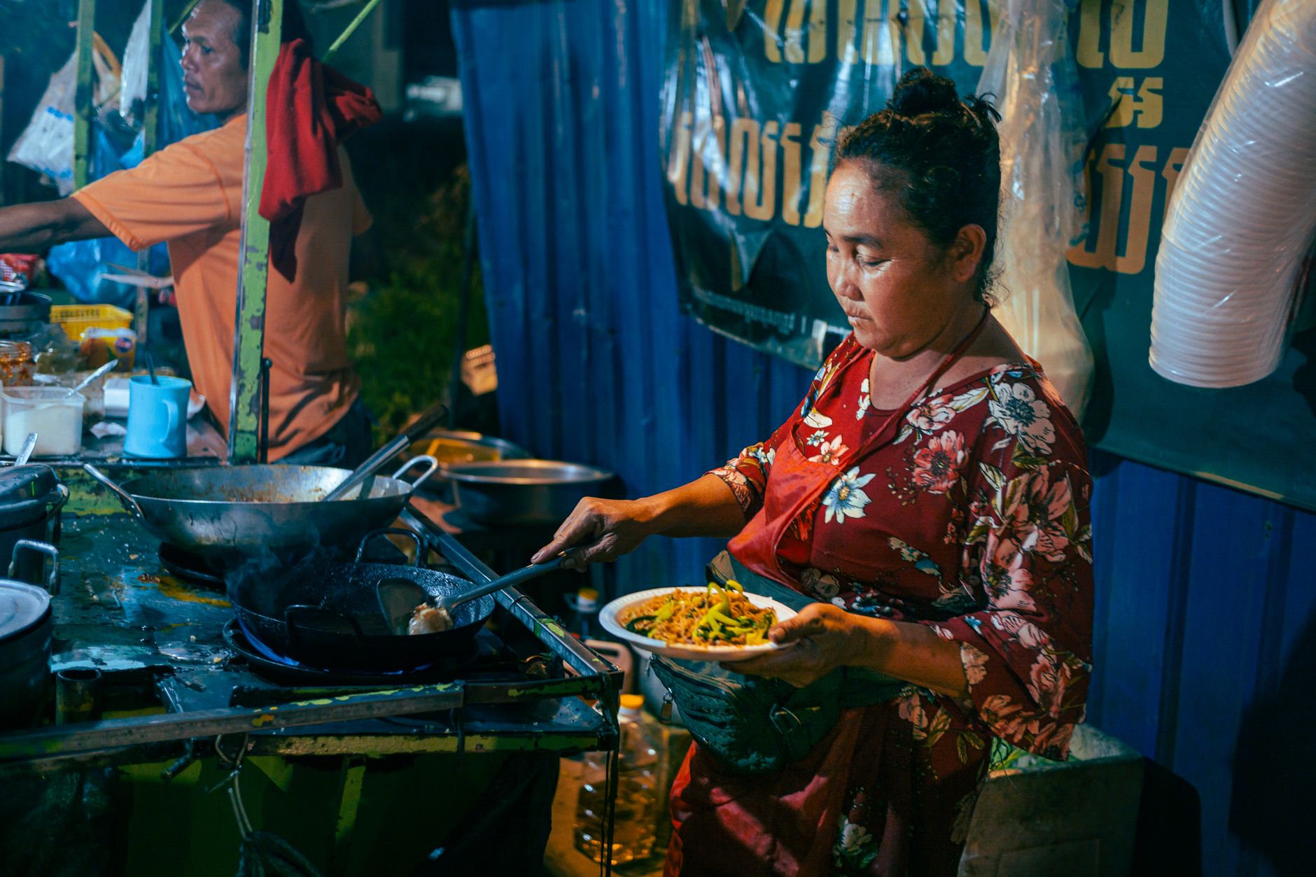 An Asian woman prepares stir-fry noodles at a vibrant street food stall during the night market.