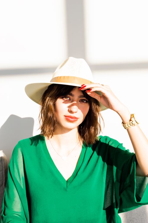 Free Elegant woman shielding eyes with hat against sun, wearing chic green blouse. Captured outdoors in Canada. Stock Photo