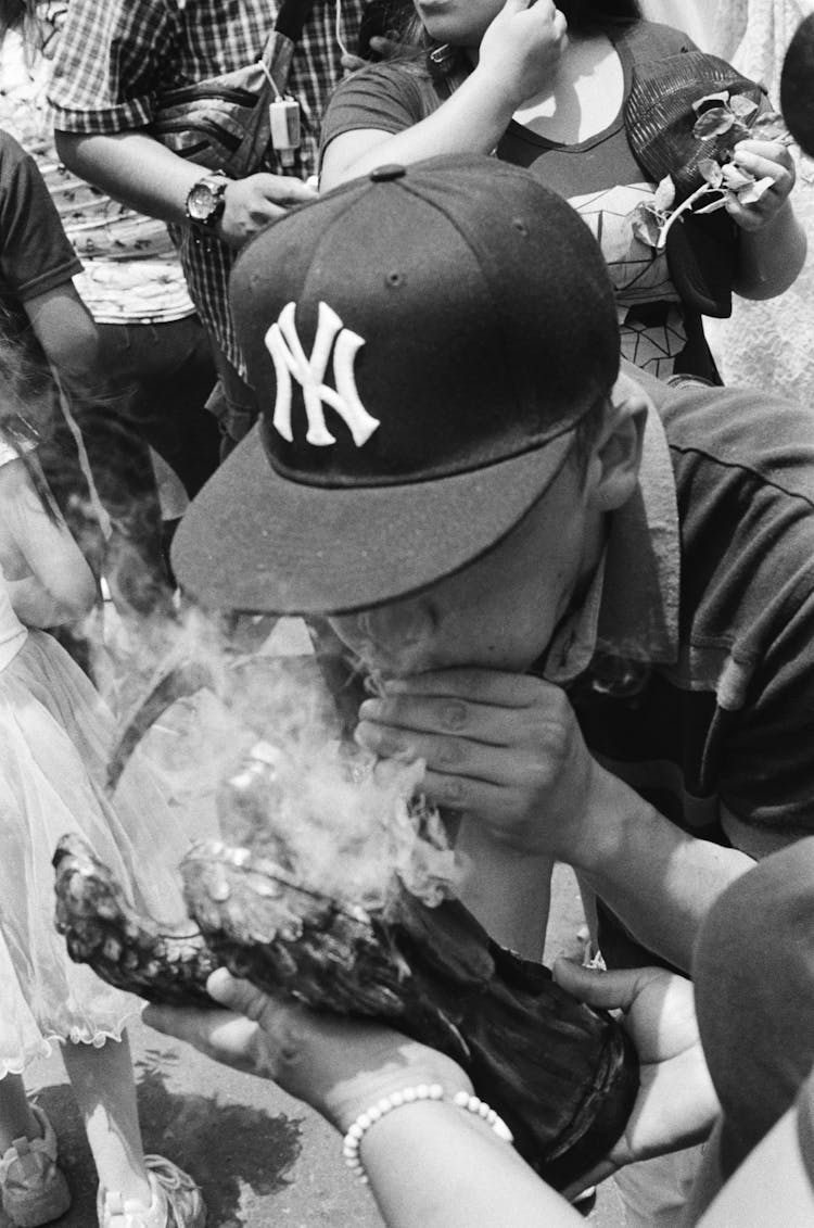 Black And White Photo Of A Man Wearing Cup Smoking In A Crowd