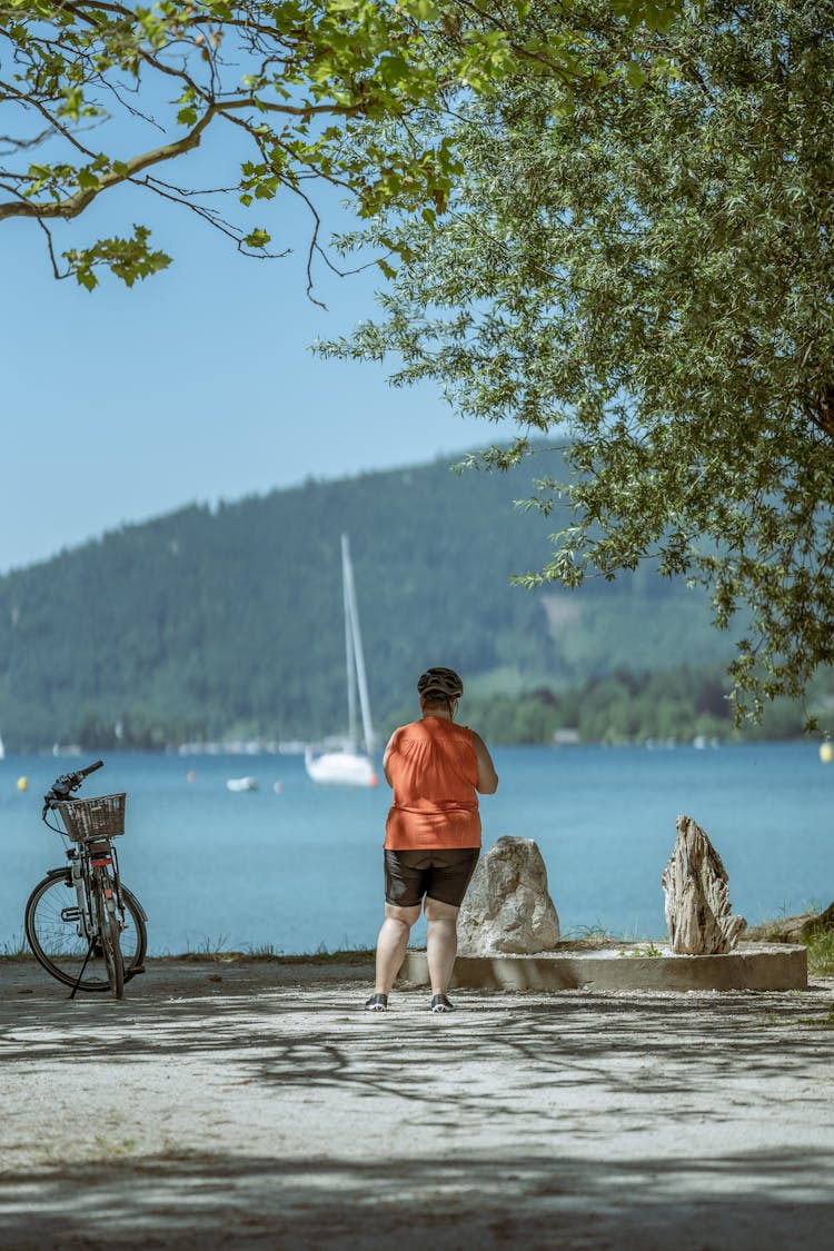 Back Of A Man Standing Under A Tree And Looking Over A Lake