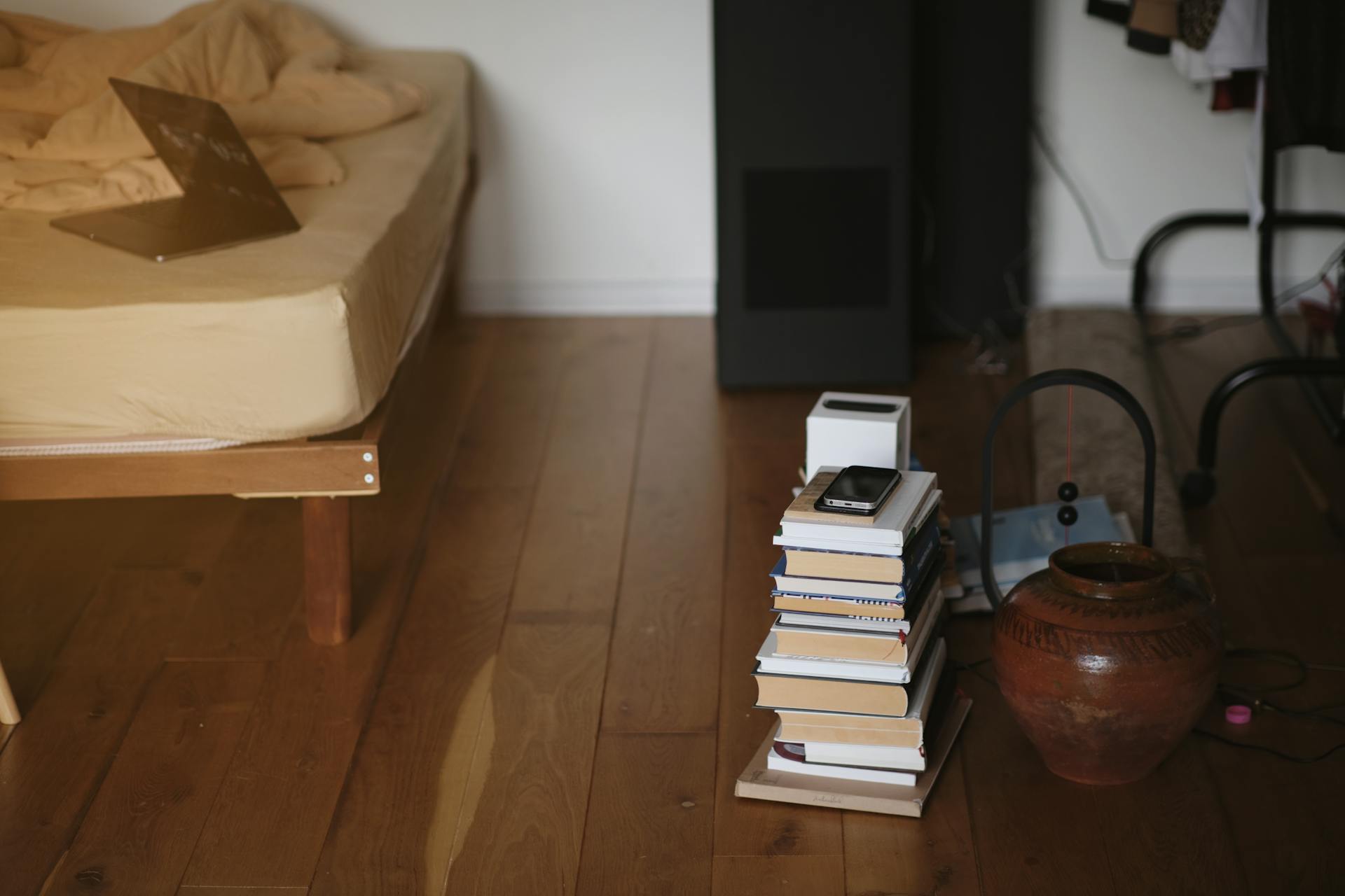 A warm and inviting bedroom with stacks of books, pottery, and a wooden bed frame.
