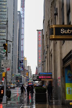 Street scene near Radio City Hall in New York with umbrellas and skyscrapers.