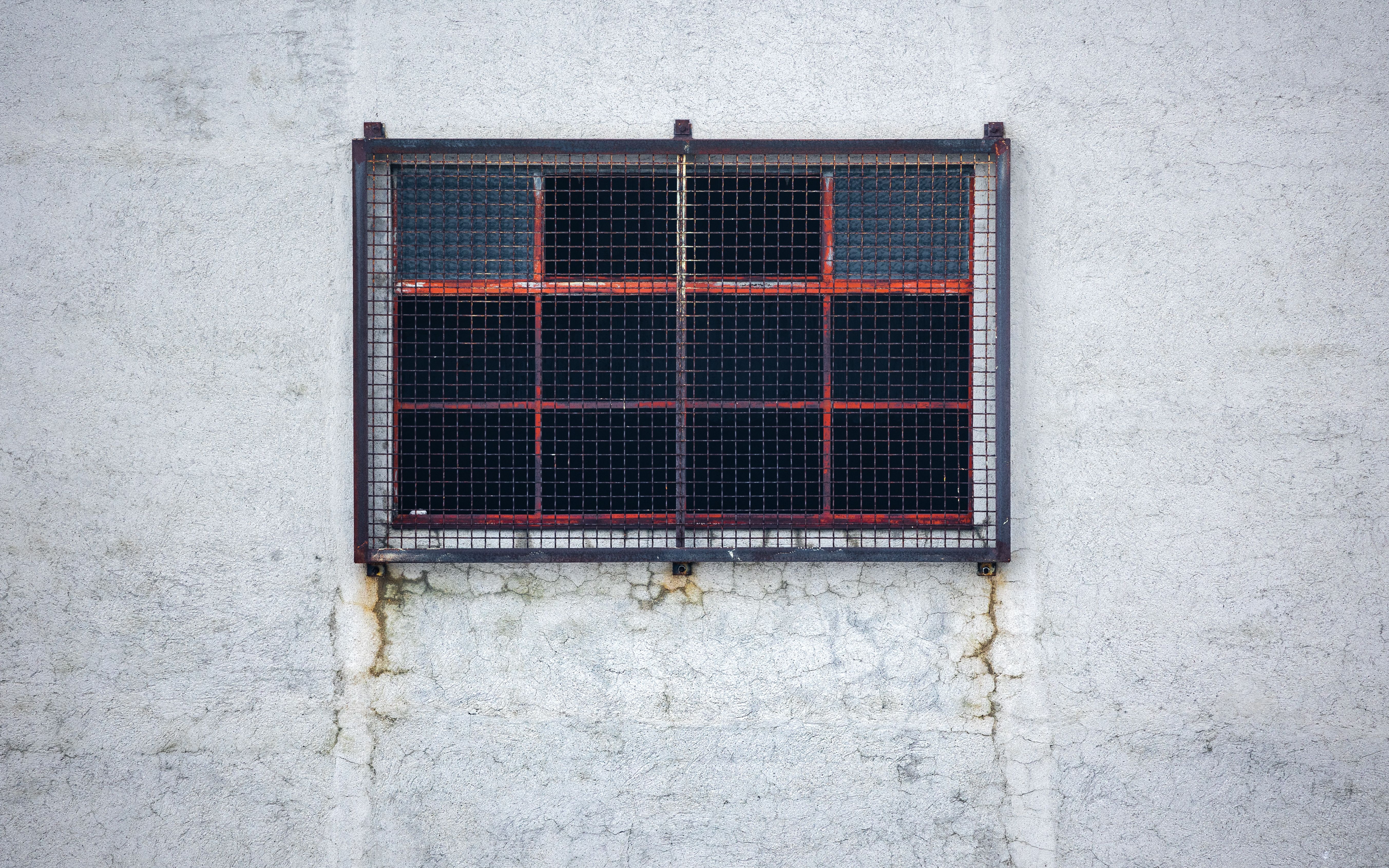 A small barred window on a weathered, cracked wall with signs of rust and age.