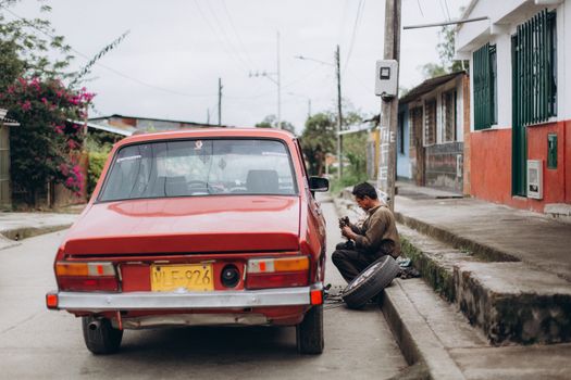 Mechanic repairing a red car on a street side in an urban neighborhood. Manual work in action.