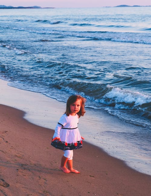 Barefooted Girl in White Dress Standing on Seashore