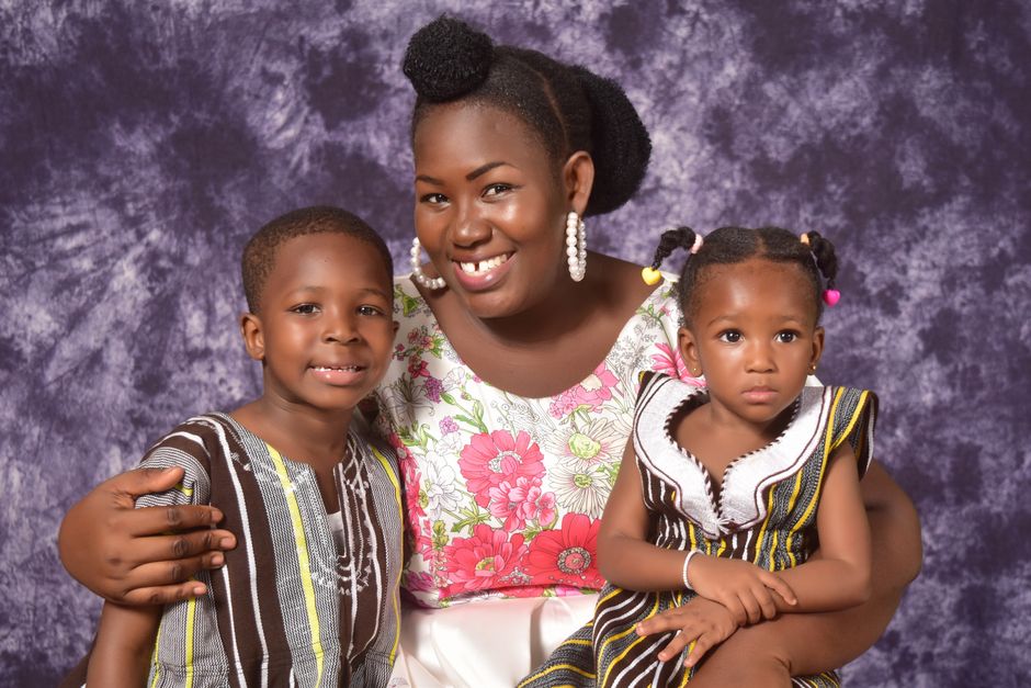 Happy African family of mother and children in traditional Ghanaian attire, radiating joy.