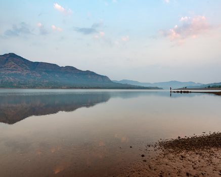 Calm waters reflecting mountains in Pune, India, at sunset—a serene natural landscape.