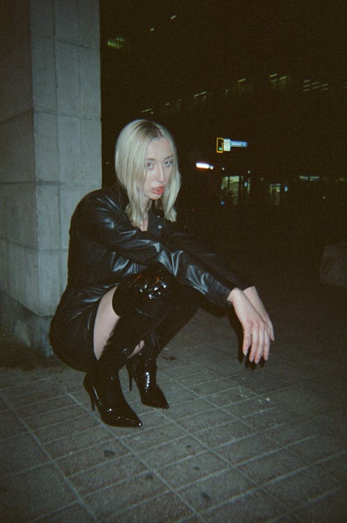 Woman in Black Leather Jacket Sitting on a Sidewalk