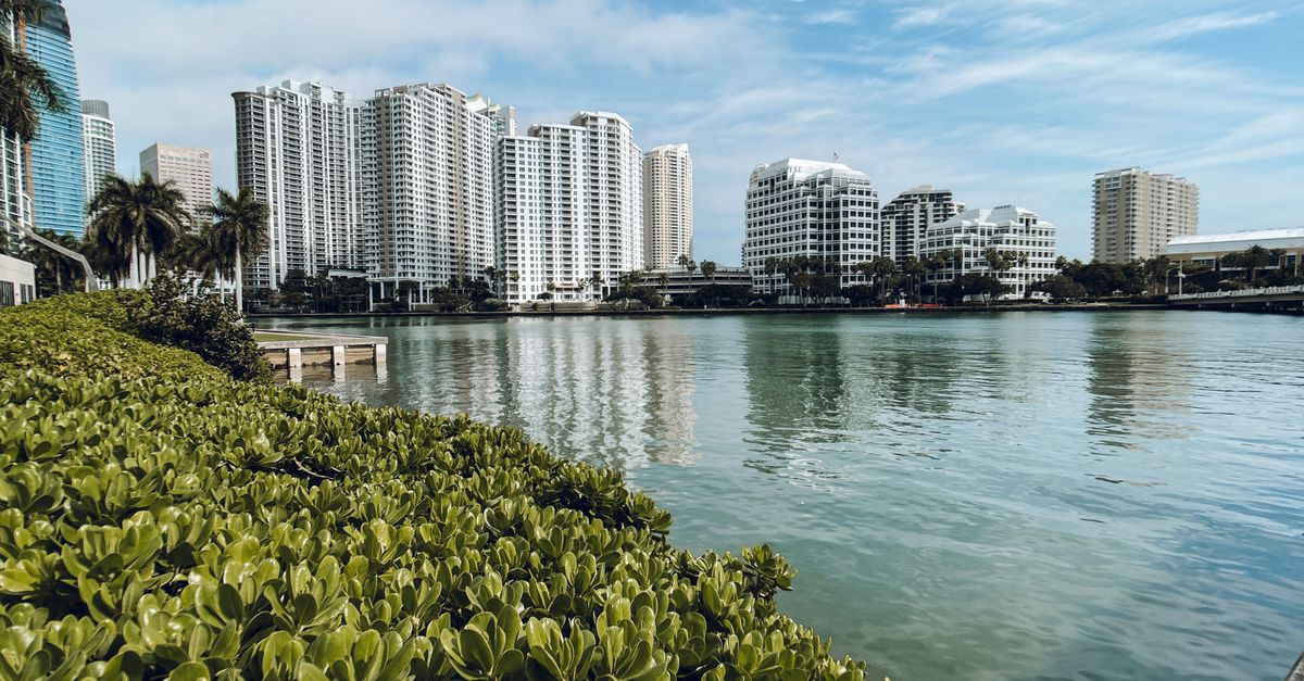 Elegant high-rise buildings reflecting in a calm river under a blue sky.
