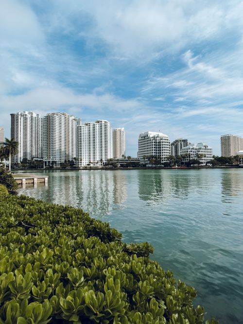 Free Modern skyline reflection in calm waters with lush greenery and blue skies. Stock Photo