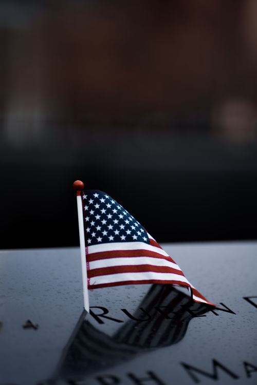 Free A small American flag placed on a reflective marble surface under a dim light, evoking patriotism. Stock Photo