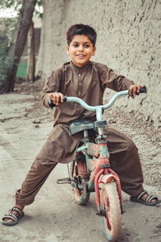 A happy child enjoys riding a bicycle on a rustic outdoor path.