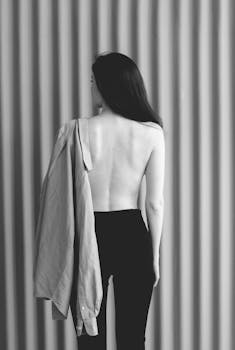 Black and white artistic photo of a woman standing with shirt loosely draped on shoulder.