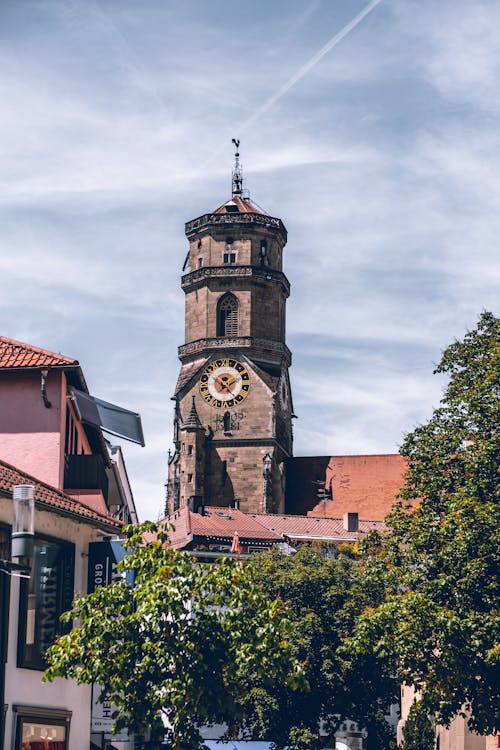 Free A Clock Tower and Buildings With Roof Tiles Near Green Trees Stock Photo