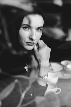 A contemplative woman in monochrome, sitting at a table with a hand on her cheek, creating a serene and introspective mood.