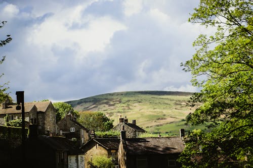 Houses and Green Trees Near a Green Hill Under a Cloudy Sky
