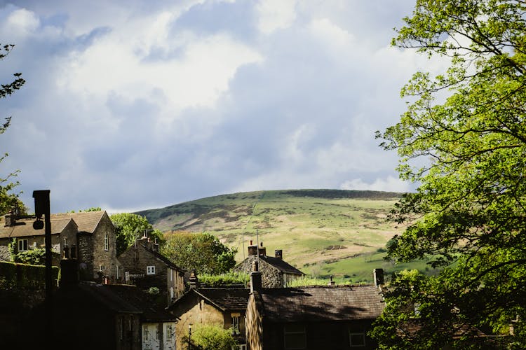 Houses And Green Trees Near A Green Hill Under A Cloudy Sky