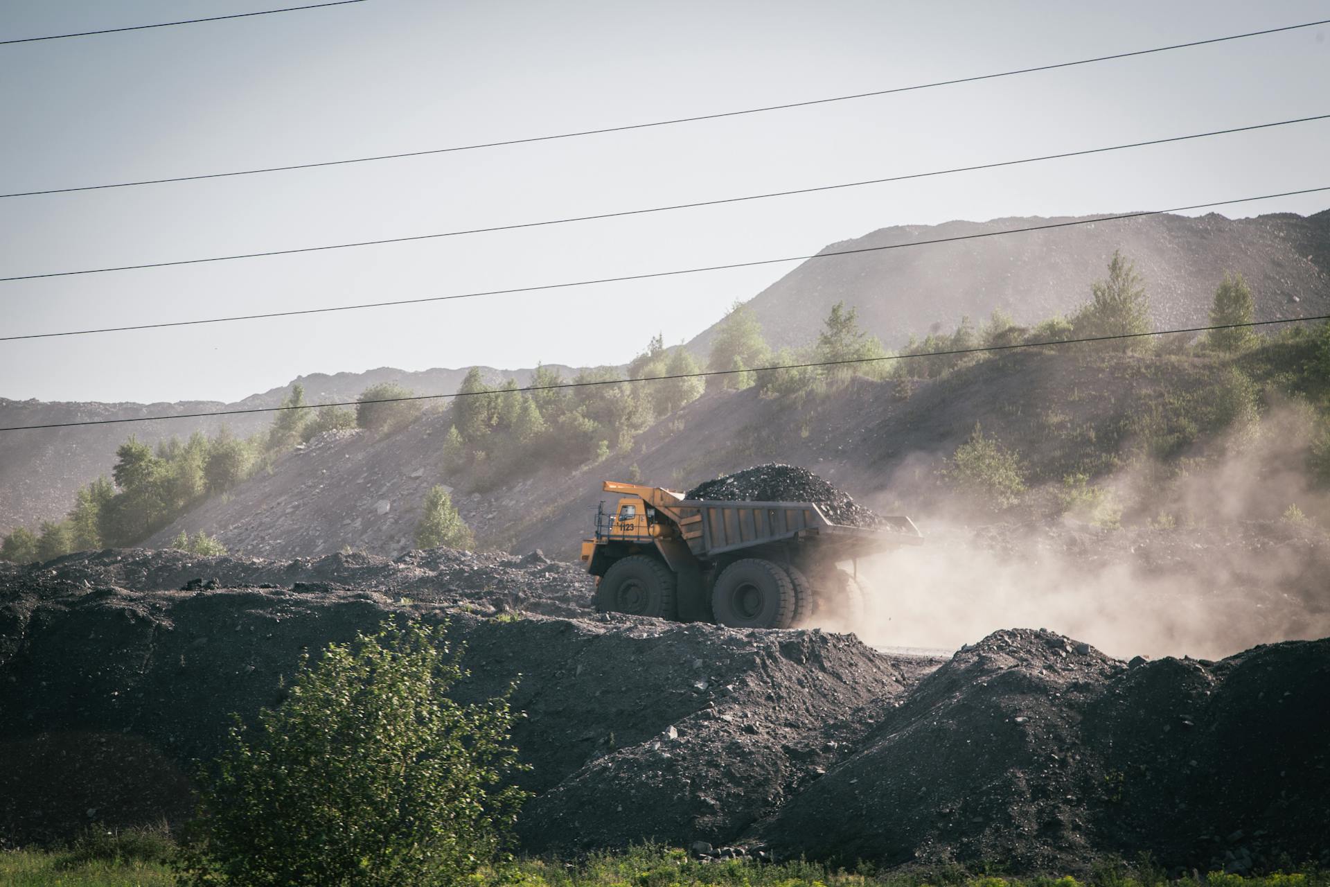 A large dump truck operates in a dusty outdoor mining site with rocky terrain.