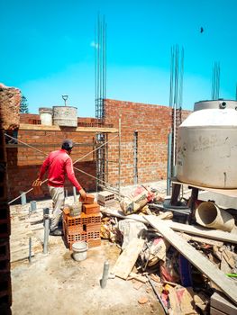 Construction worker arranging bricks on a sunny building site with scaffolding and materials.