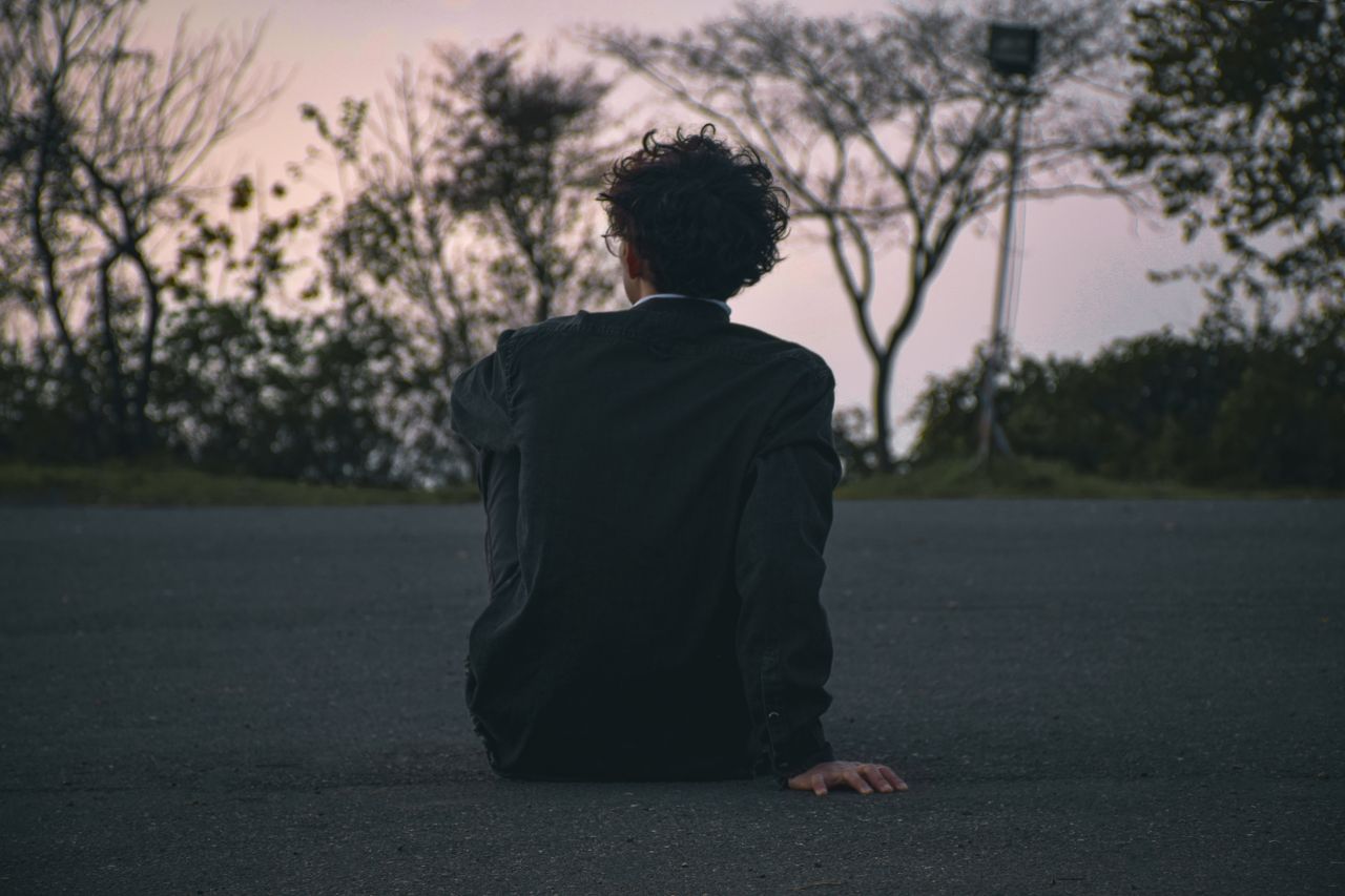 a man with curly hair sits on a road in solitude at dusk offering a co