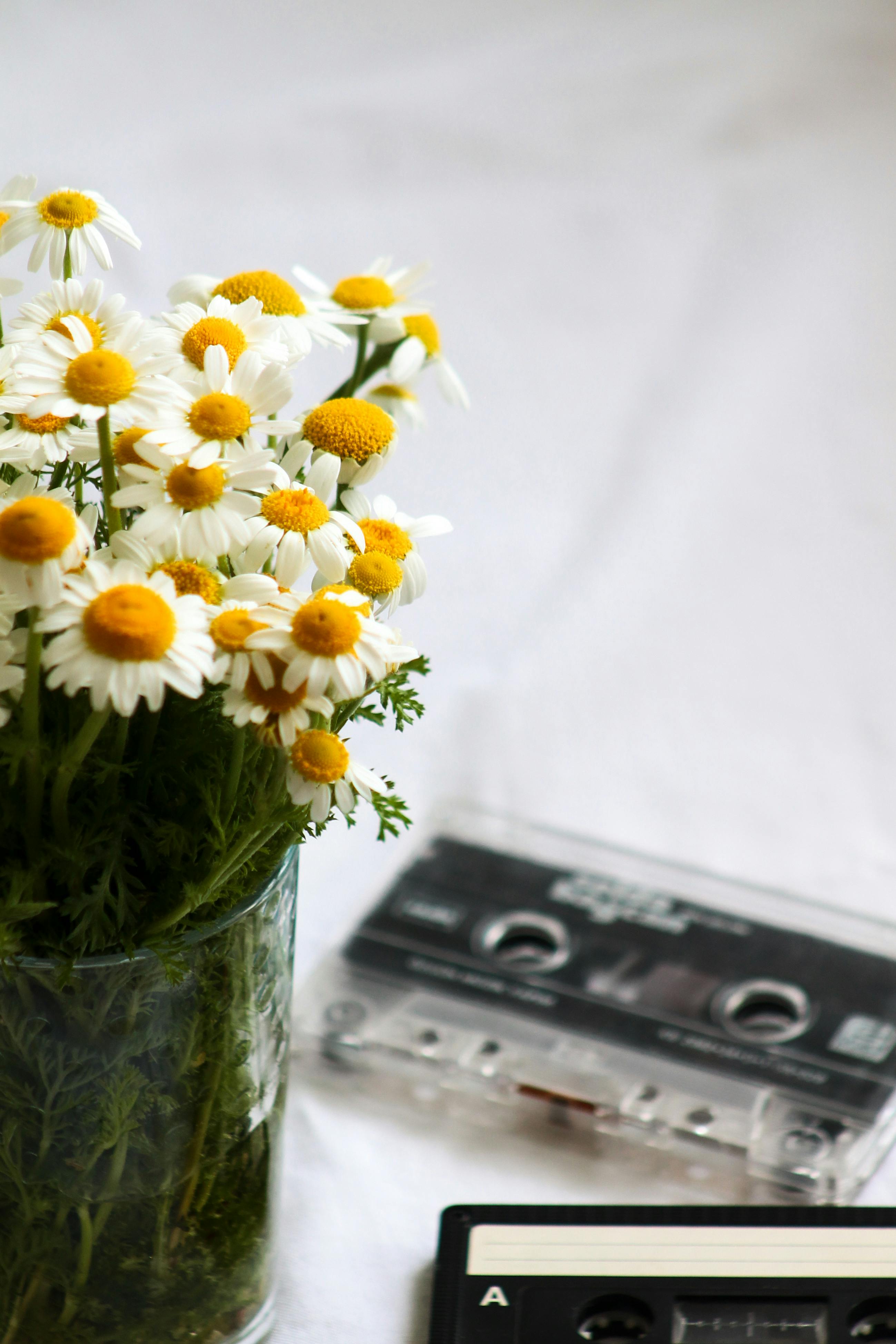 a bouquet of daisy flowers in a vase beside casette tapes