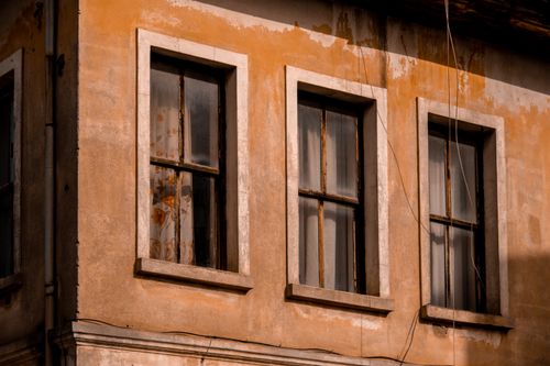 Free A sunlit building facade with three rustic, weathered windows showcasing vintage architecture. Stock Photo
