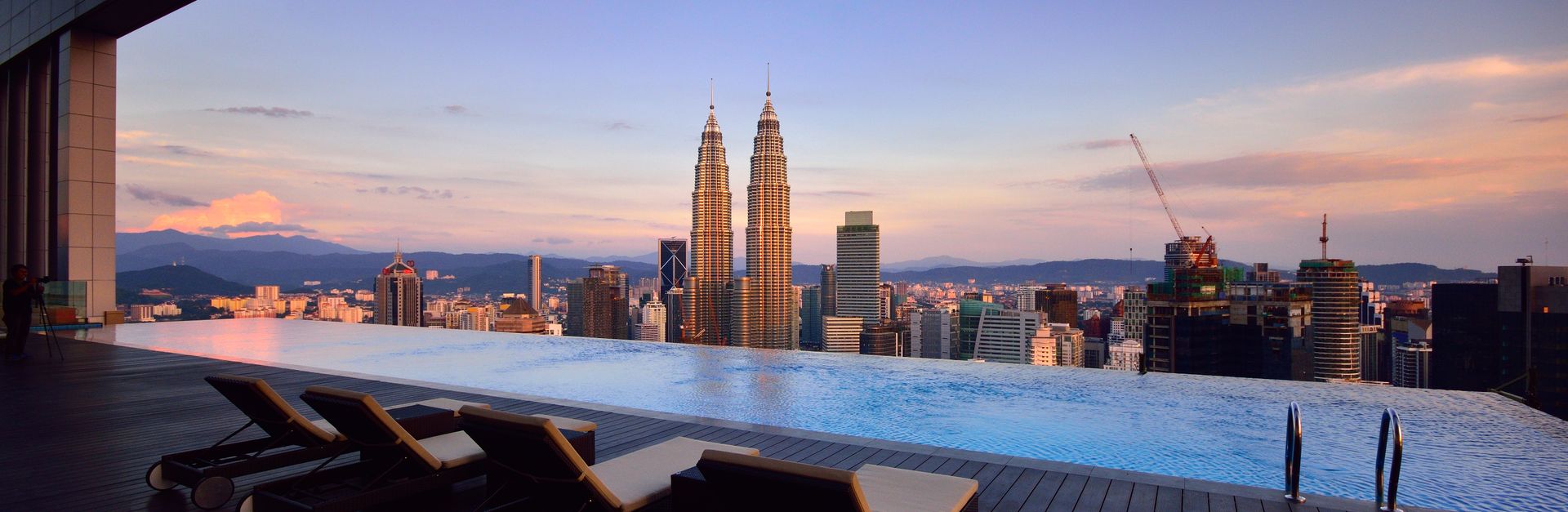 Relax by a luxury infinity pool with stunning Kuala Lumpur skyline and Petronas Towers at twilight.