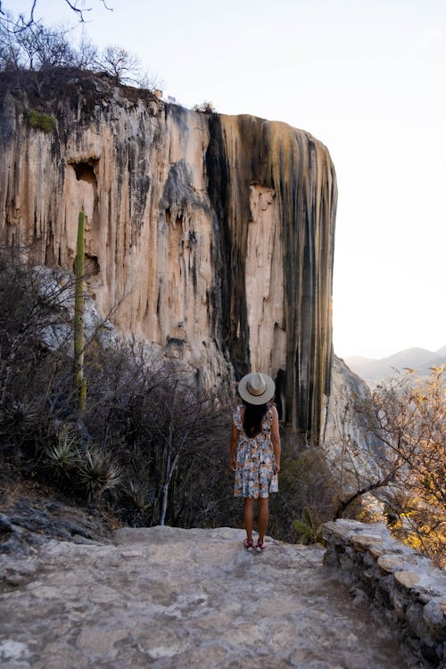 Woman in Floral Dress and Hat Standing Near Rock Formation