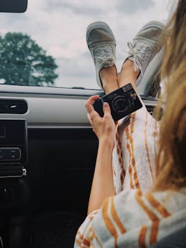 Woman Holding Compact Camera While Feet On Top Of Vehicle Dashboard