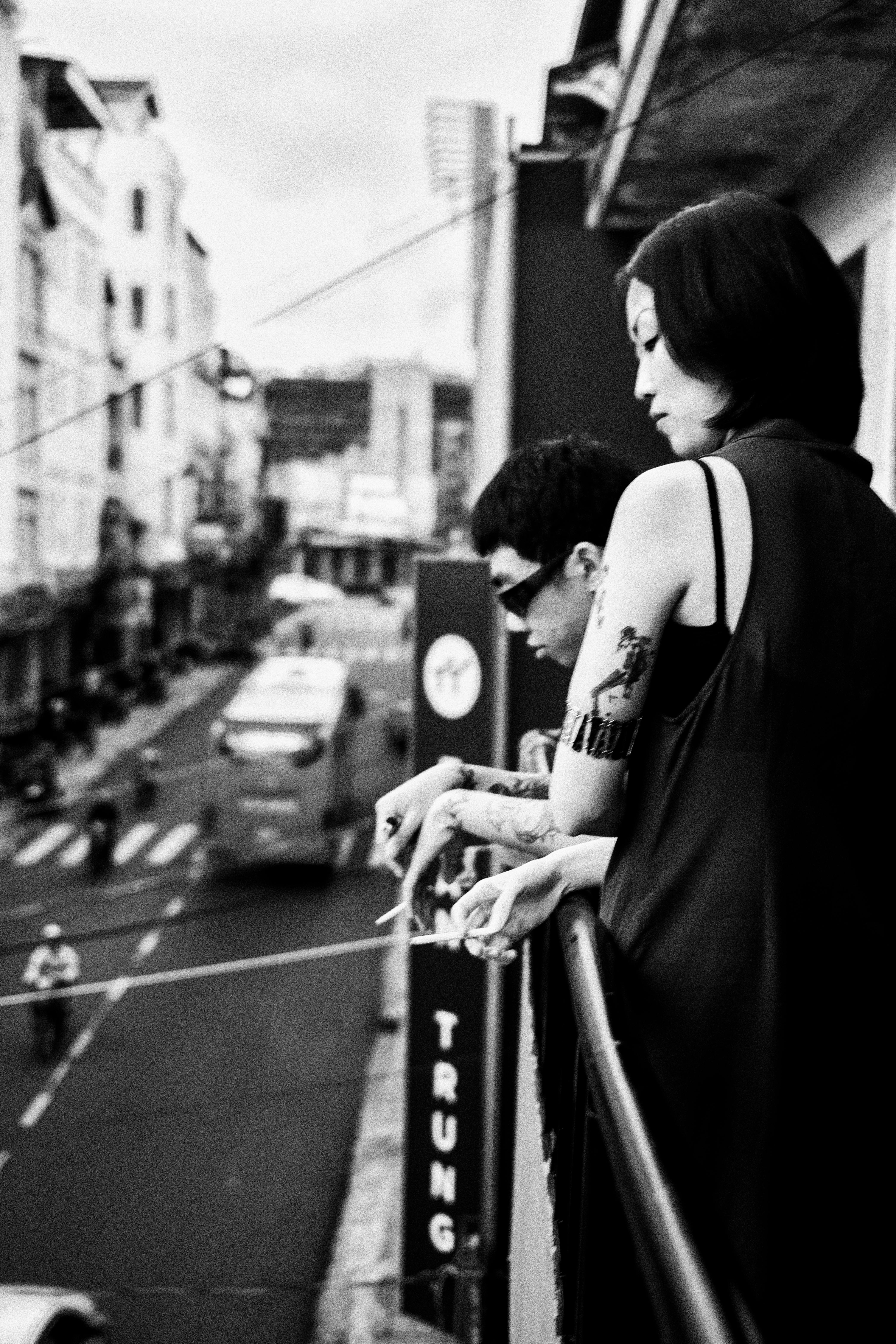 Black and white urban scene with people on a balcony overlooking city street.