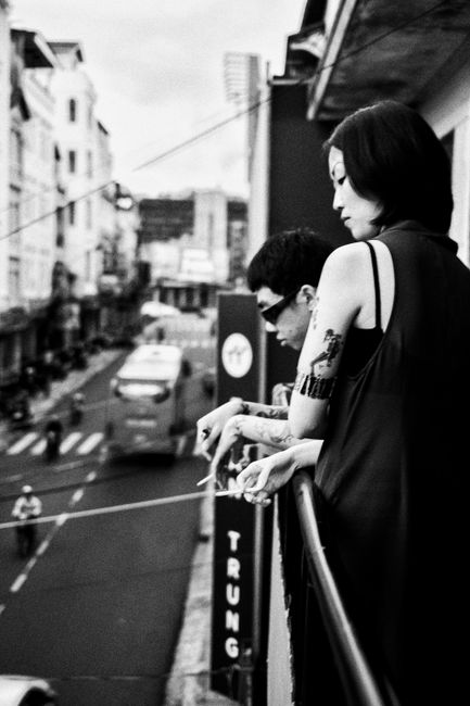 Black and white urban scene with people on a balcony overlooking city street.