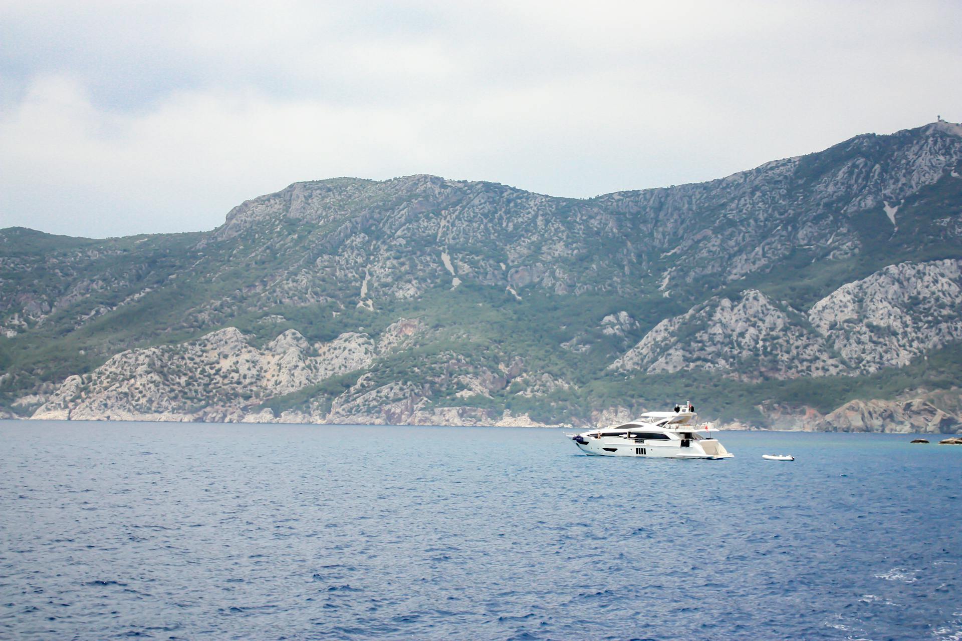 Luxurious yacht cruising along a scenic coastline framed by rugged mountains and clear blue waters.