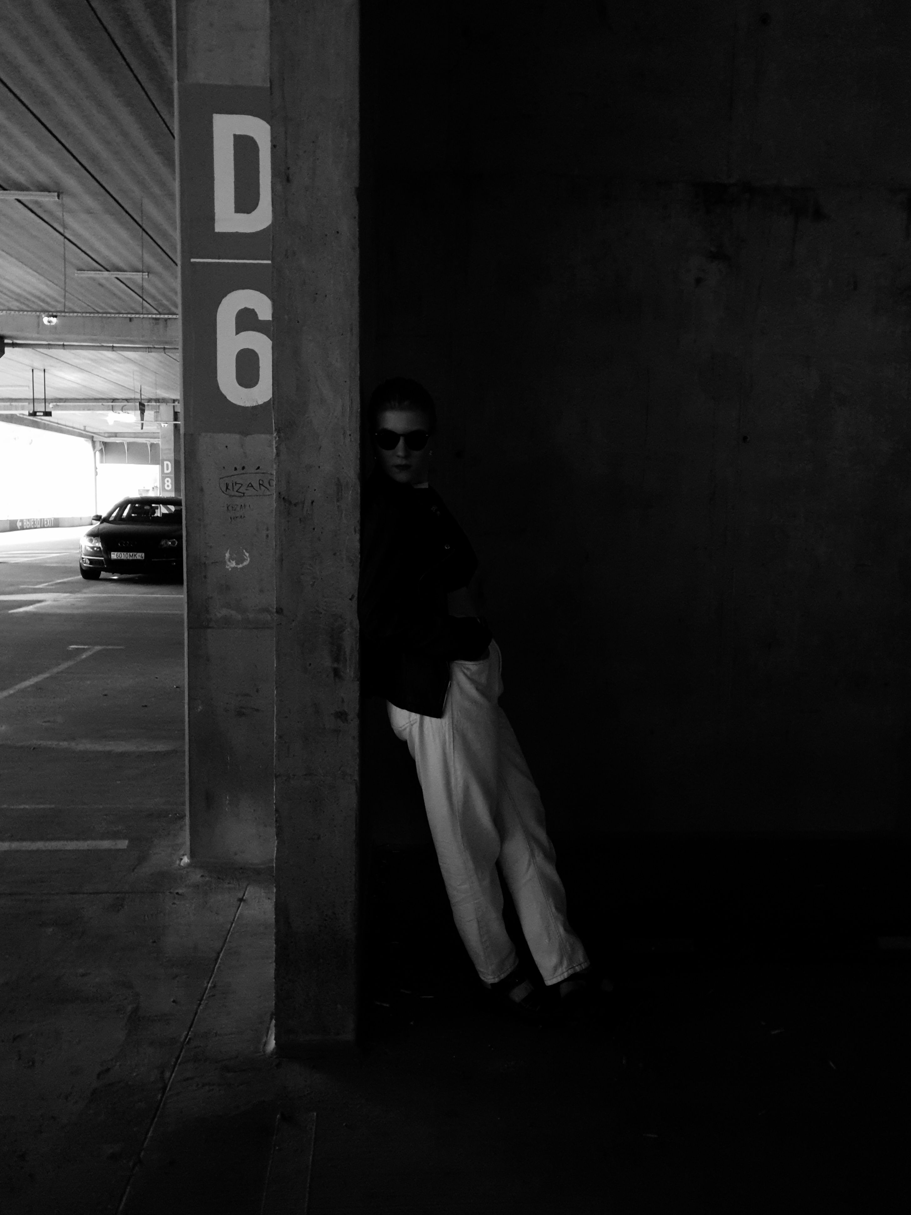 Grayscale Photo of Man in Black Jacket and White Pants Leaning on Wall ...