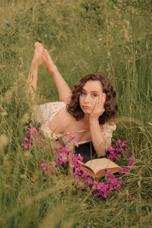 Woman in Floral Dress Lying on Grass Field with a Book