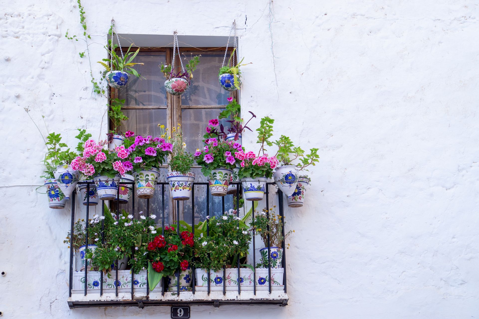 Vibrant flower pots decorate a balcony in Jávea, Spain, showcasing Spanish ceramic artistry.