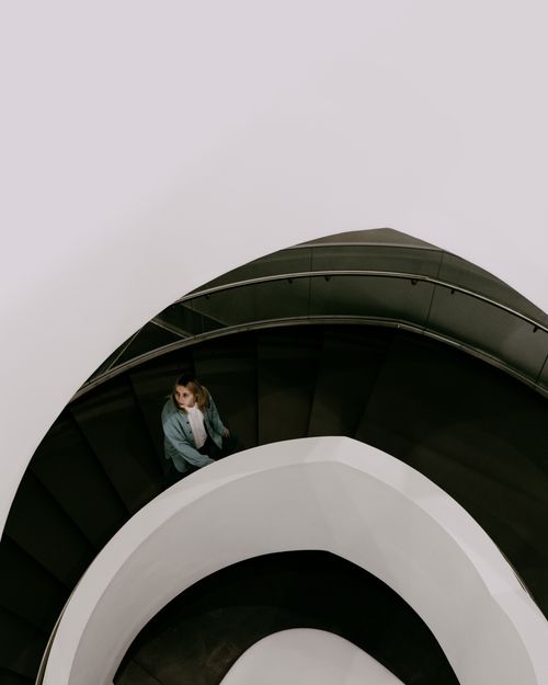 Free A woman ascends an elegant spiral staircase in a modern architectural setting. Stock Photo