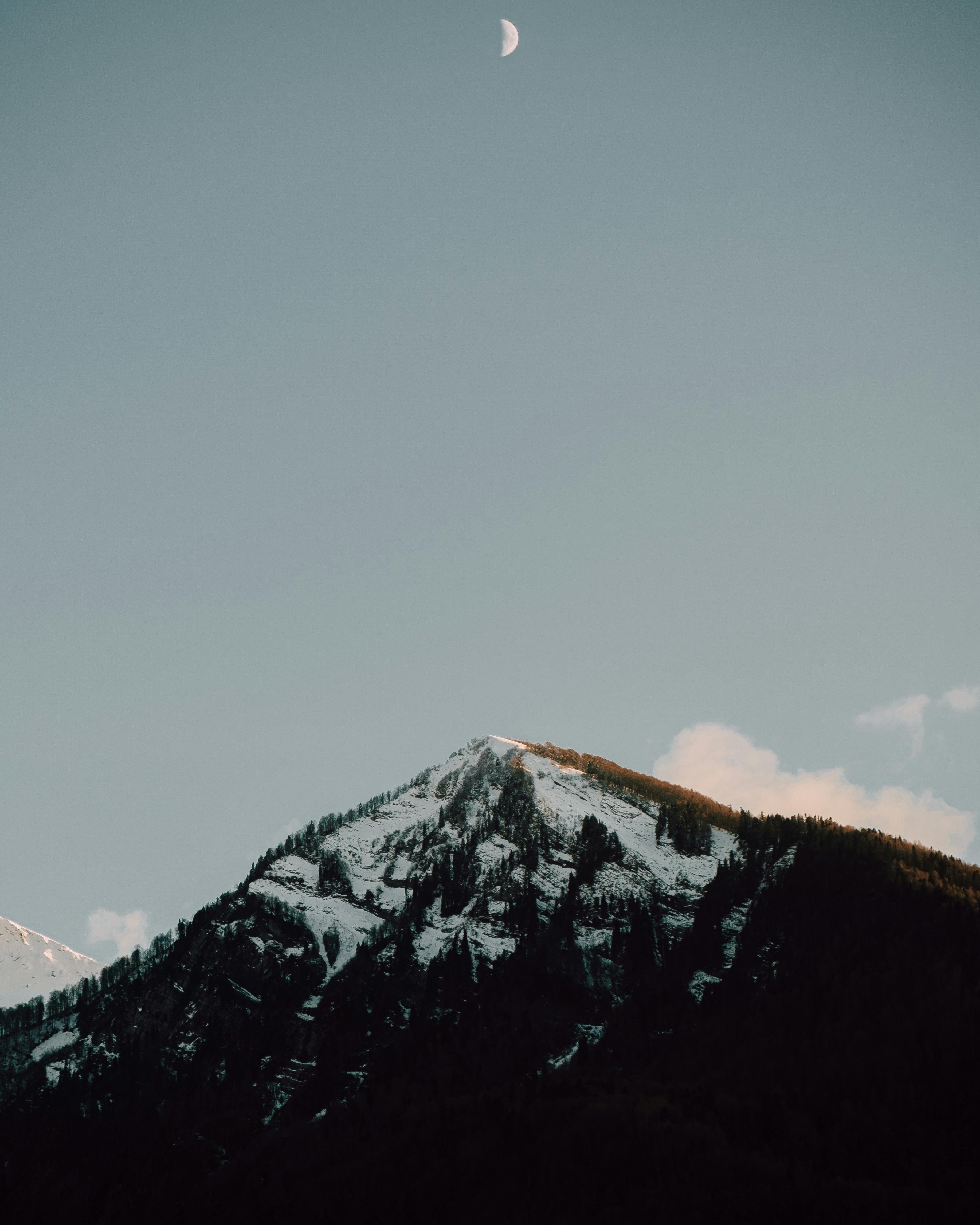 A serene view of a snow-covered mountain under a crescent moon with a clear sky.