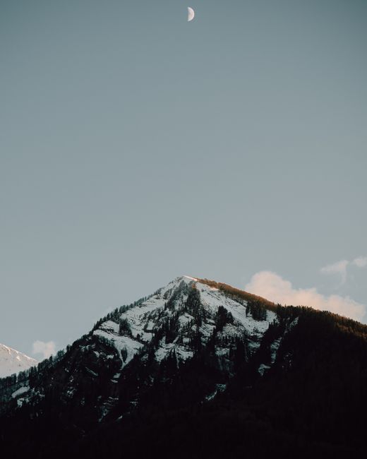 A serene view of a snow-covered mountain under a crescent moon with a clear sky.