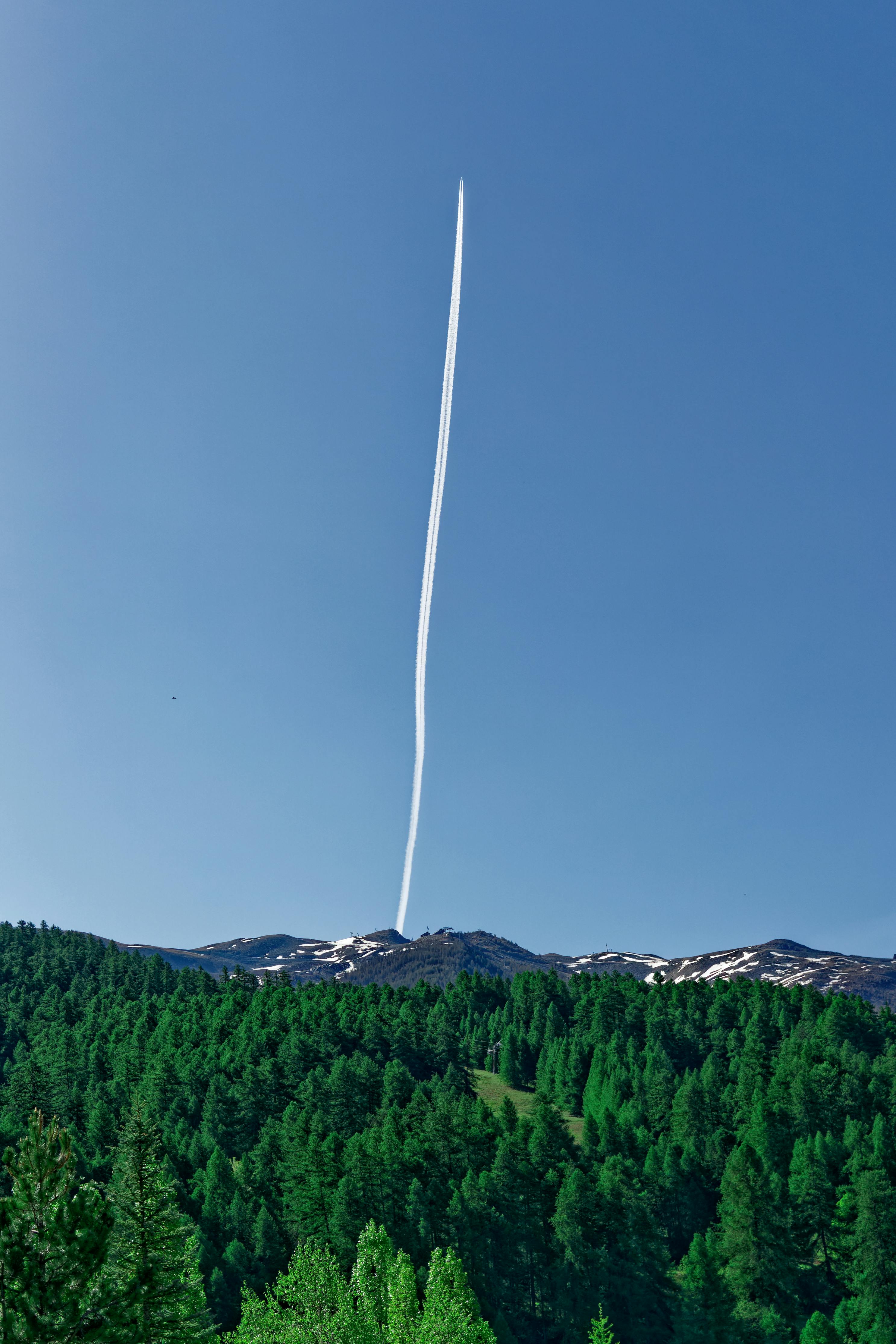 A striking contrail in a clear blue sky above a dense green forest in Provence, France.