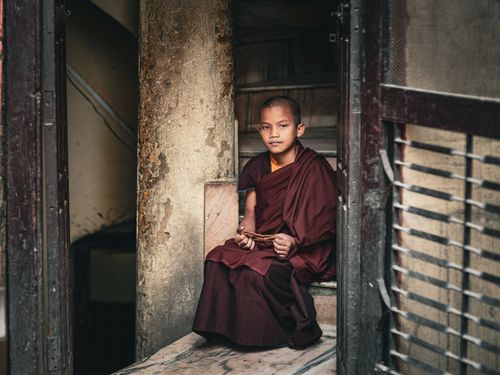 Free A young Buddhist monk in traditional robes meditates indoors on a staircase, exuding tranquility. Stock Photo