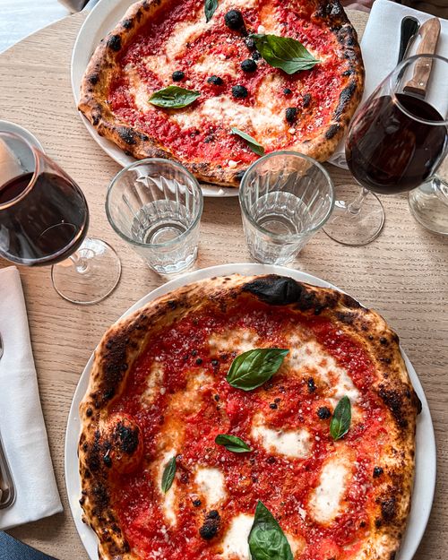 Free Two classic Margherita pizzas with red wine on a wooden table setting. Stock Photo