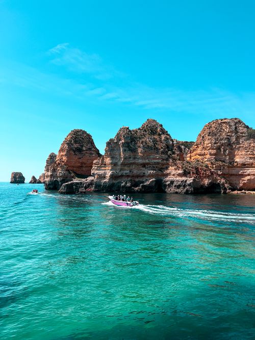 Free Vibrant coastal view of rock formations with boats passing by, under a clear blue sky. Stock Photo