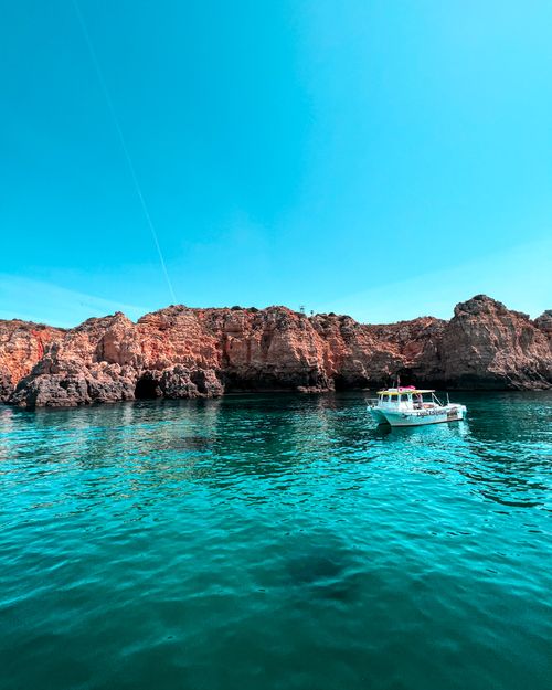 Free Bright seaside view of rocky cliffs and a yacht on turquoise water under clear skies. Stock Photo