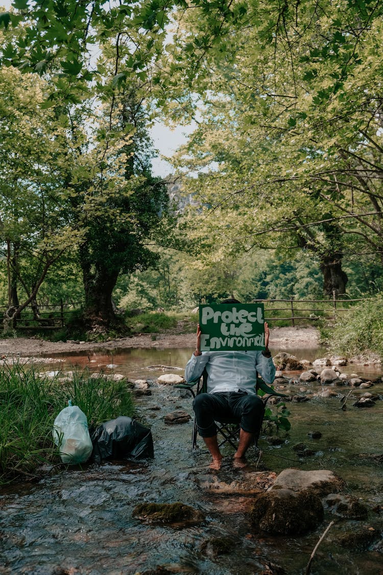 A Person Sitting On Chair Holding A Protect The Environment Placard