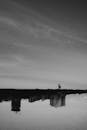 Grayscale Photo of Man Standing on Dock