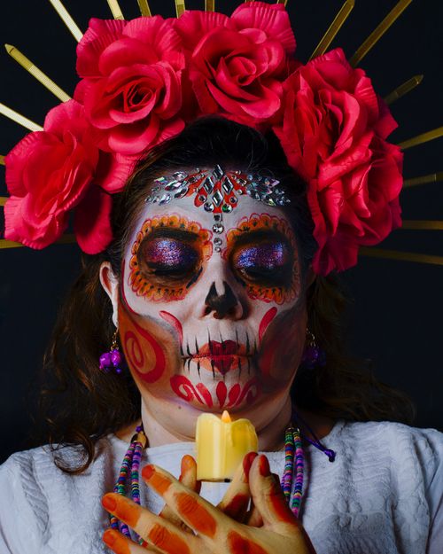 Free Colorful Day of the Dead Catrina with floral headdress holding a candle, embracing tradition. Stock Photo