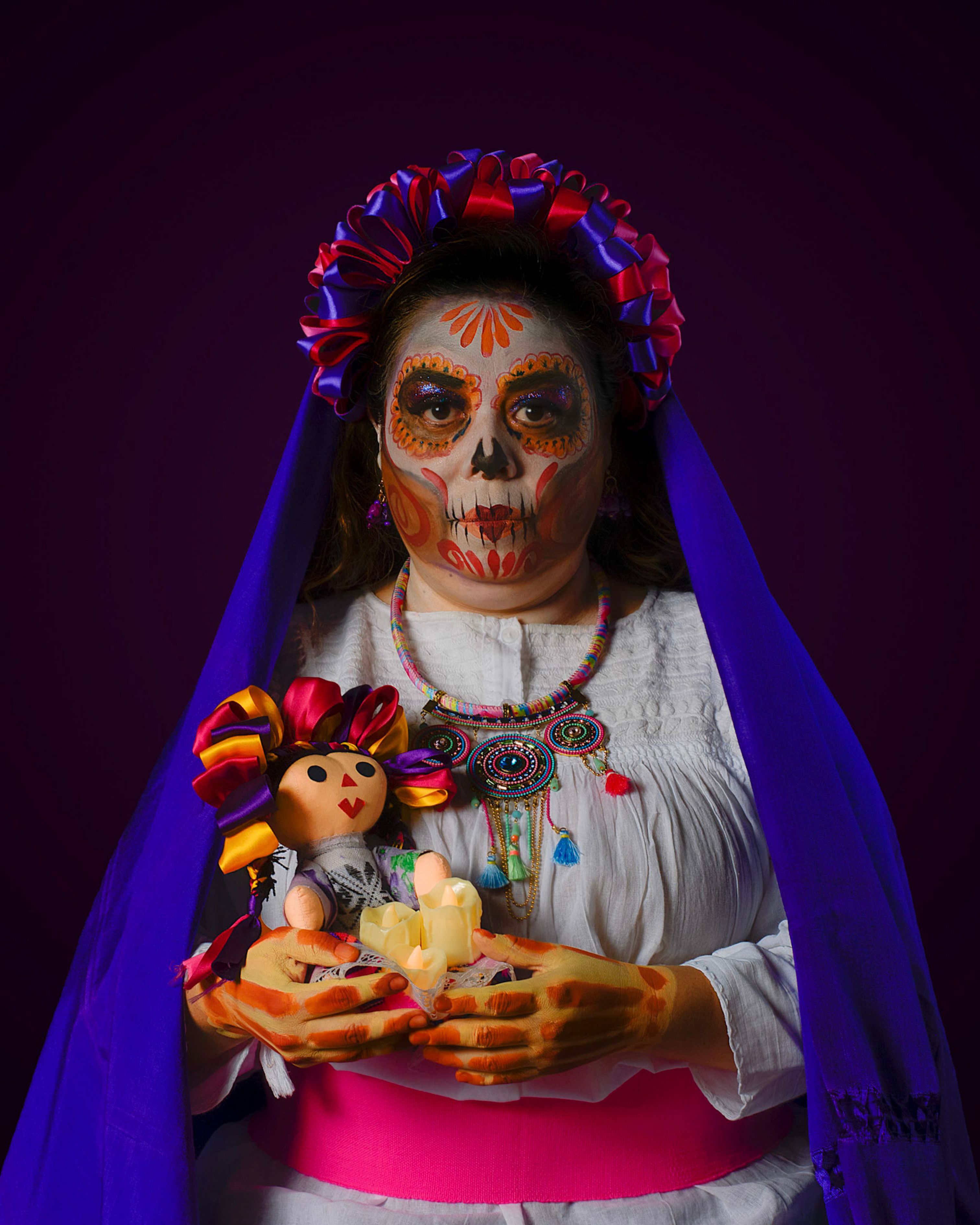 Woman in Dia de los Muertos attire with face paint and traditional doll in Mexico City.