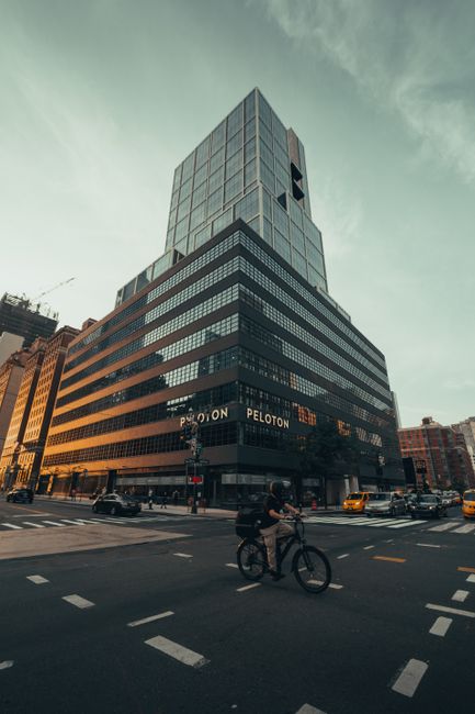 Cyclist crossing street in New York, featuring the Peloton building during daytime.