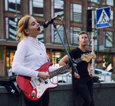 A woman playing electric guitar and singing with a microphone outdoors.